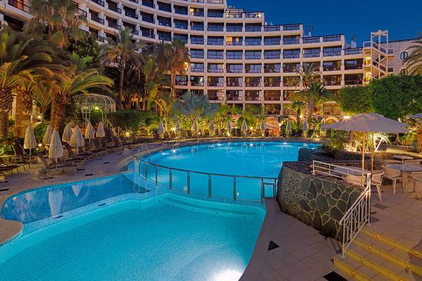 Abendansicht des Swimmingpools im Seaside Sandy Beach Hotel mit illuminierten Gebäuden und Sonnenliegen.