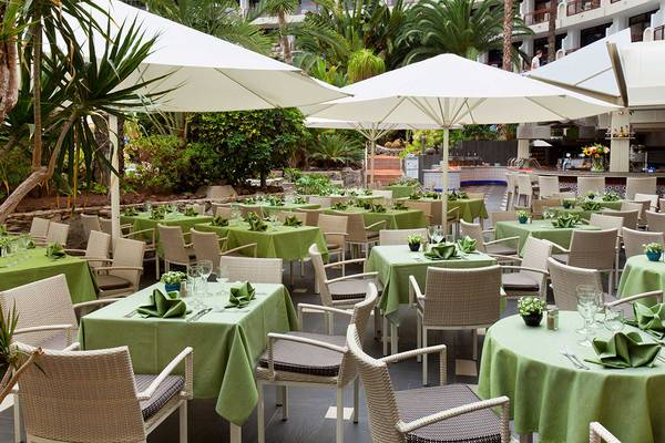 Außenbereich des Seaside Sandy Beach Hotels mit gedeckten Tischen und Stühlen unter Schirmen.