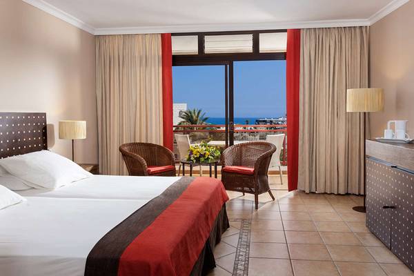 Doppelzimmer mit Meerblick im Seaside Sandy Beach Hotel, mit zwei Betten, zwei Korbstühlen und einem großen Fenster.