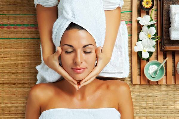 Frau im Spa-Salon mit einem Handtuch auf dem Kopf, die eine Gesichtsmassage genießt.