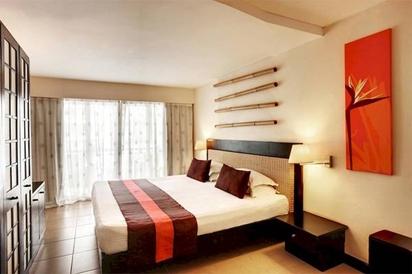Doppelbett im Schlafzimmer im Pearle Beach Resort & Spa mit braunen Kissen und weißer Bettwäsche.