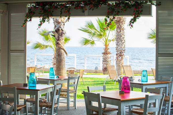 Außenbereich des Aquamare Beach Hotel & Spa mit Tischen, Stühlen und Blick auf das Meer.