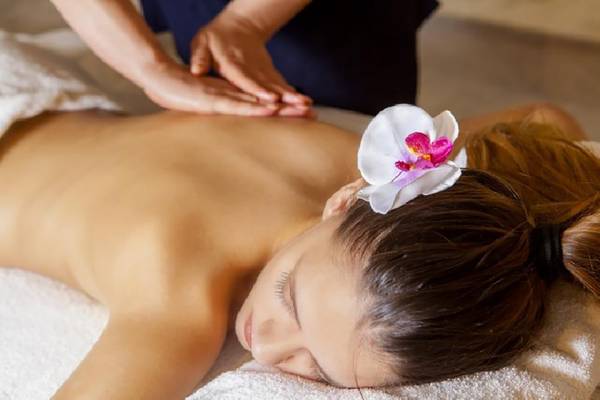 Eine Frau genießt eine Massage im Aquamare Beach Hotel & Spa, mit einer Blume im Haar und geschlossenen Augen.