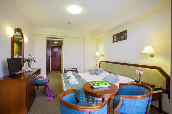 Innenansicht eines Doppelzimmers im Aquamare Beach Hotel mit Bett, Tisch, Stühlen und Fernseher.