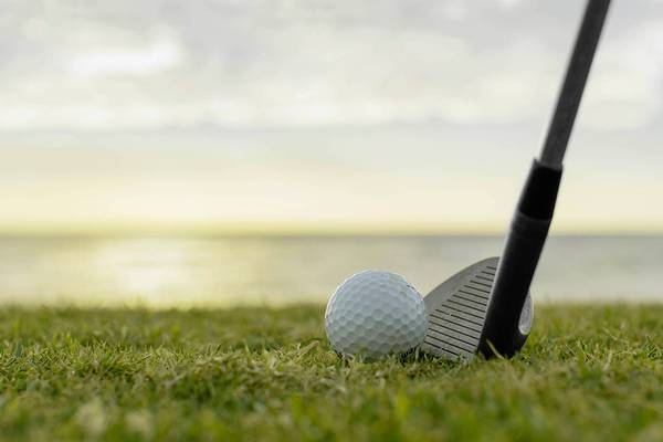 Golfschläger trifft einen Golfball auf einem Rasenfeld mit Meer im Hintergrund