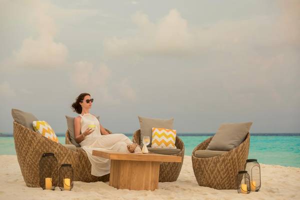 Eine Frau sitzt auf einer Sitzgelegenheit am Strand des Fushifaru Maldives Hotels.