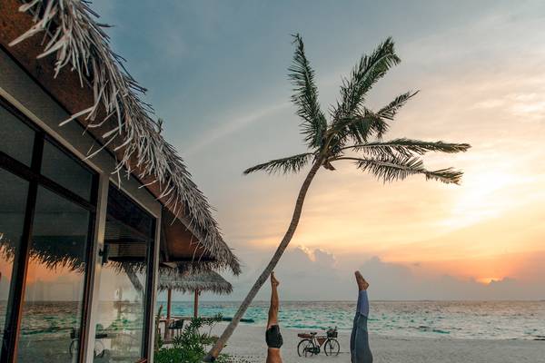 Zwei Personen praktizieren Yoga auf einem Holzdeck am Strand des Fushifaru Maldives.