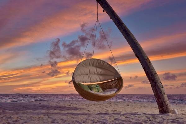Ein hängendes Bett von Fushifaru Maldives auf dem Strand bei Sonnenuntergang.