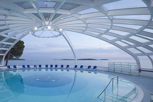 Ein runder Pool im Freien mit blauen Liegen und einer Aussicht auf das Meer, im Zora Hotel.
