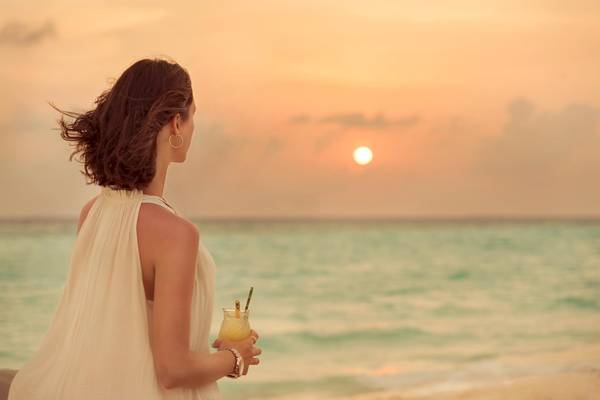 Frau am Strand bei Sonnenuntergang im Fushifaru Maldives, das Hotel steht im Hintergrund.