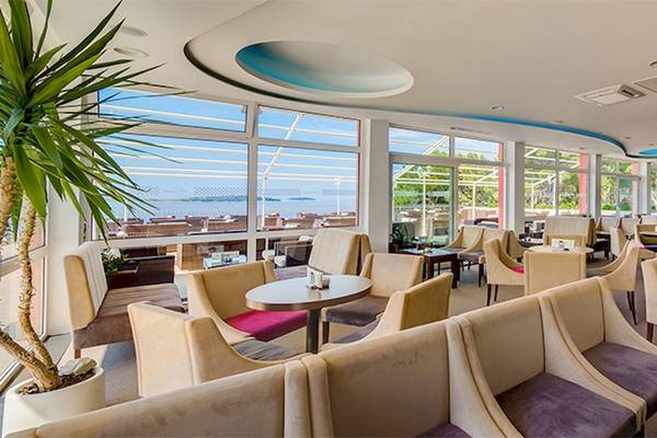 Innenansicht des Loungebereichs im Zora Hotel mit großen Fenstern und Blick auf den Ozean.