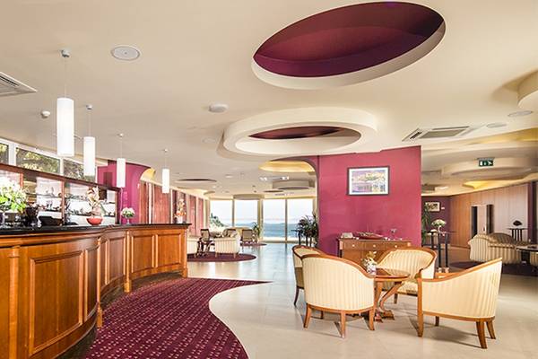 Innenansicht der Rezeption des Zora Hotels mit rotem Teppich, Holzmöbeln und Blick auf den Ozean.