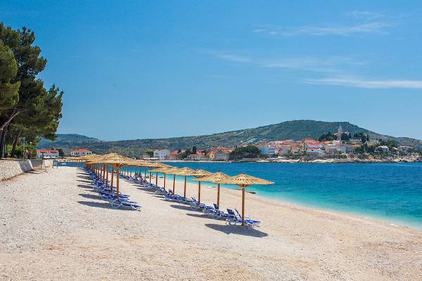 Strand des Zora Hotels mit Sonnenschirmen und Liegestühlen vor einem kleinen Dorf