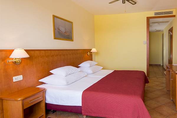 Innenansicht eines Doppelzimmers im Zora Hotel mit zwei Betten, gelben Wänden und einem Fernseher.