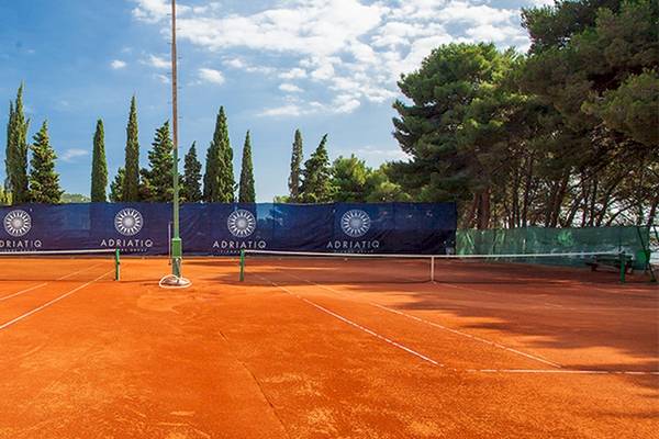 Tennisplatz im Zora Hotel mit blauen Bannern und Bäumen im Hintergrund.