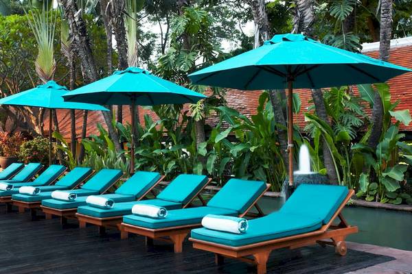 Reihe von blauen Liegestühlen unter türkisen Sonnenschirmen im Anantara Riverside Bangkok Resort