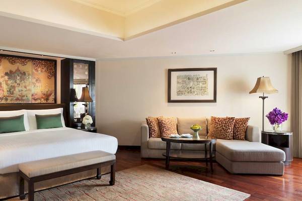 Ein elegantes Zimmer im Anantara Riverside Bangkok Resort mit einem großen Bett, einem Sofa und einer Tischlampe.