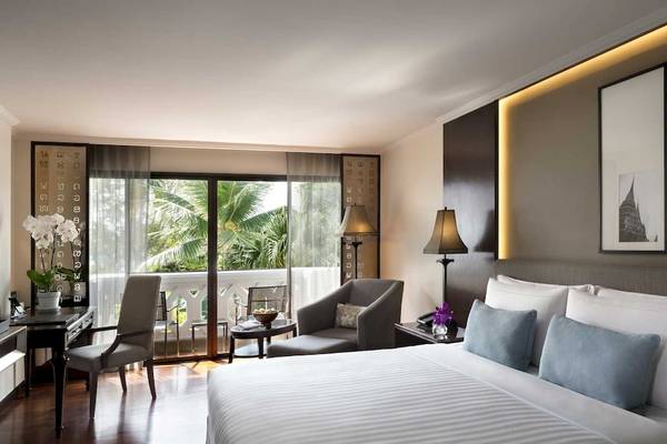 Schlafzimmer im Anantara Riverside Bangkok Resort mit großem Bett, Kissen und Blick auf den Garten.