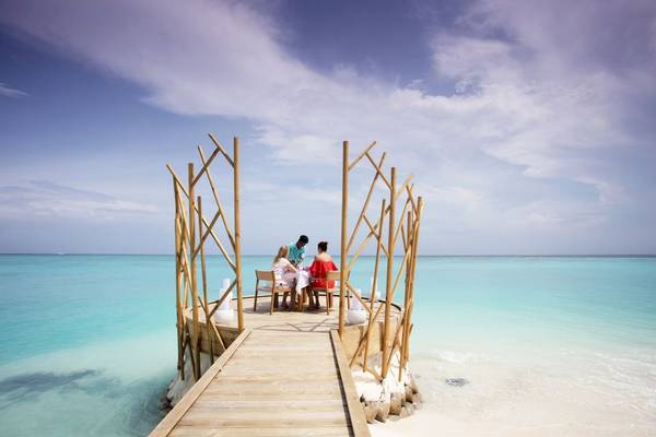 Essen auf der Insel im Fushifaru Maldives mit drei Personen, umgeben von blauem Wasser und einem hölzernen Pavillon.