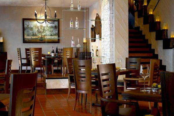 Innenansicht des Restaurants im Anantara Riverside Bangkok Resort mit Holztischen, Stühlen und einem Kronleuchter.
