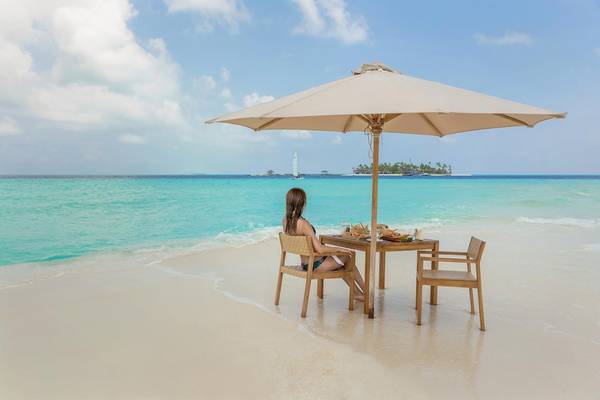 Frau sitzt unter einem Sonnenschirm auf einem Tisch am Strand von Fushifaru Maldives