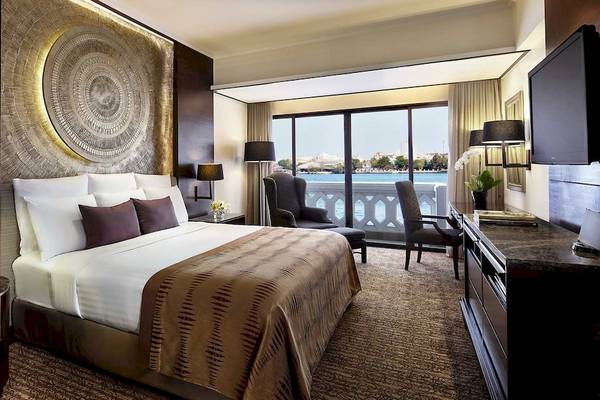 Innenansicht eines Zimmers im Anantara Riverside Bangkok Resort mit Bett, Möbeln und Blick auf den Fluss.