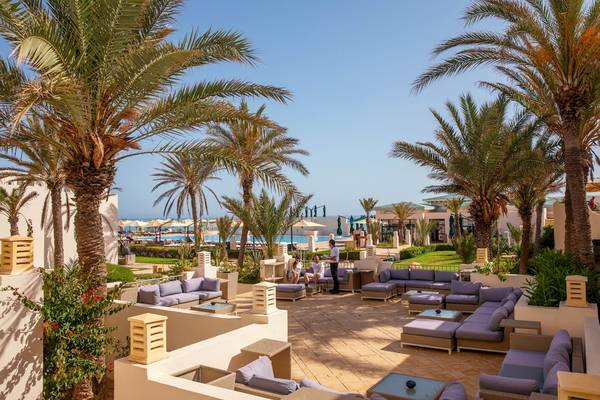 Außenterrasse des Ulysse Djerba Thalasso & Spa Hotels mit Palmen, Loungemöbeln und Blick auf das Meer.