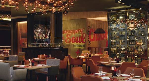 Innenraum des Mövenpick Hotel Jumeirah Beach Restaurant mit bunten Wandmalereien, Tischdekoration und hängenden Kronleuchtern.