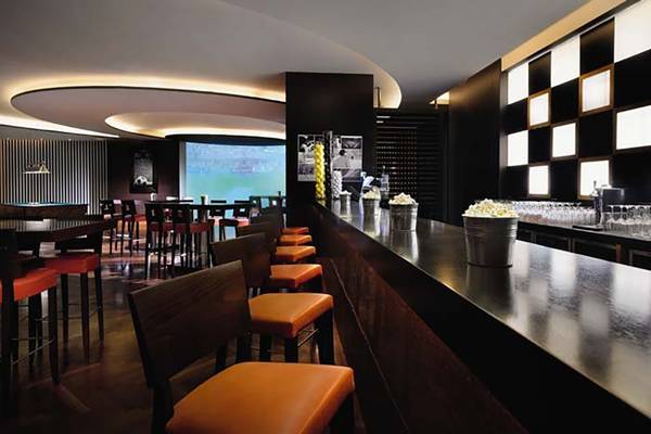 Innenansicht der Bar im Mövenpick Hotel Jumeirah Beach mit roten Stühlen und einer großen Leinwand.