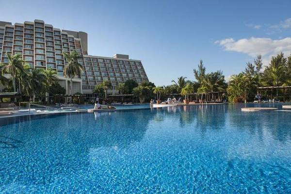 Ein großer Swimmingpool mit Palmen und einem Hotelgebäude im Hintergrund.