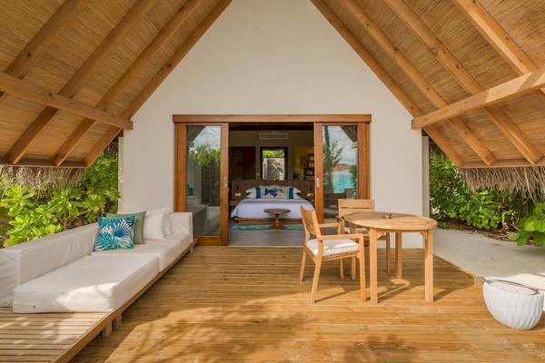 Innenansicht einer Villa im Fushifaru Maldives mit Terrasse, Couch, Tisch und Schlafzimmer.
