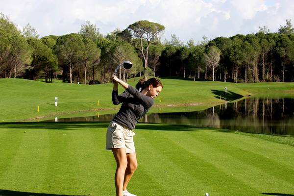 Eine Frau schlägt einen Golfball auf einem Golfplatz ab, umgeben von Bäumen und Wasserhindernissen.