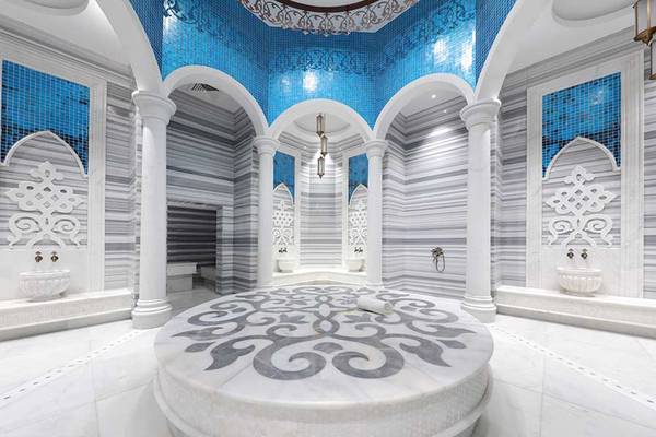 Innenbereich der Sauna im Sueno Hotels Deluxe Belek mit weißen und grauen Marmor, blauen Mosaiken und vier Waschbecken.