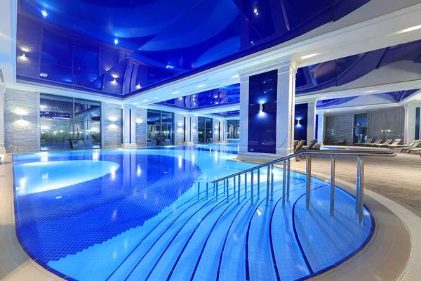 Innenpool im Sueno Hotels Deluxe Belek mit blauen Fliesen und modernen Handläufen.