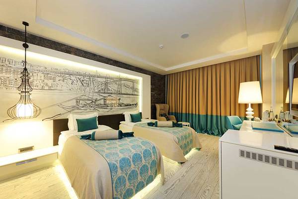 Doppelbettzimmer im Sueno Hotels Deluxe Belek mit blauer Bettwäsche und Stadtmotivwand