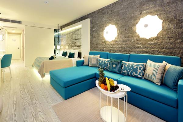 Suite im Sueno Hotels Deluxe Belek mit blauem Sofa, Tisch, Obstteller und Bett