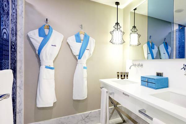 Badezimmer der Sueno Hotels Deluxe Belek mit zwei weißen Bademänteln und blauen Accessoires.