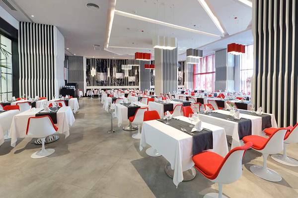 Innenbereich eines Restaurants im Sueno Hotels Deluxe Belek mit Tischdecken und roten Stühlen.