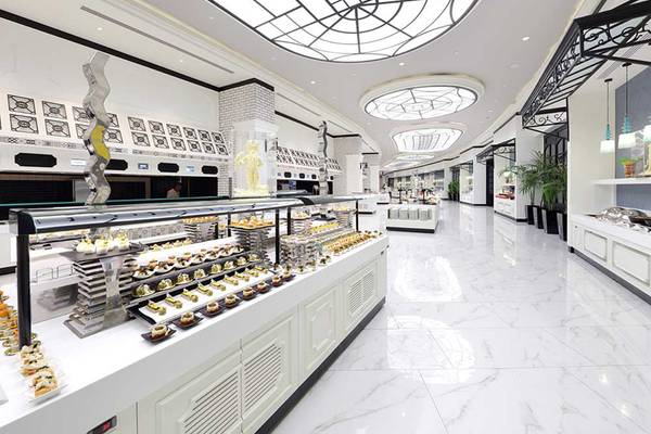 Innenbereich eines eleganten Restaurants im Sueno Hotels Deluxe Belek mit Marmorboden, Glasdecken und einer Theke voller Desserts.
