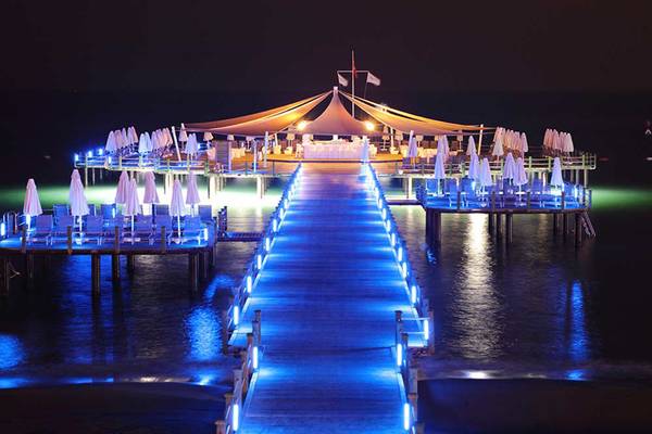 Beleuchtete Terrasse des Sueno Hotels Deluxe Belek bei Nacht mit Pavillon und blauen Lichtern.