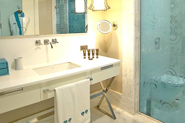 Badezimmer im Sueno Hotels Deluxe Belek mit weißer Theke, Glasdusche und Marmorboden.