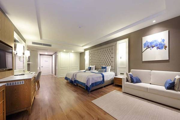 Suite-Zimmer im Sueno Hotels Deluxe Belek mit zwei Betten, Couch, Fernseher und Gemälde.