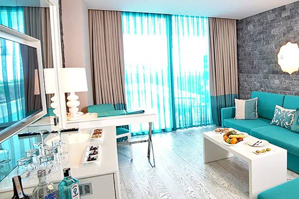 Das elegante Zimmer im Sueno Hotels Deluxe Belek mit türkisfarbener Couch, weißen Möbeln und moderner Einrichtung.