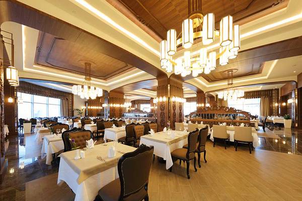 Innenansicht des Restaurants im Sueno Hotels Deluxe Belek mit gedeckten Tischen, Holzboden und Kronleuchtern.