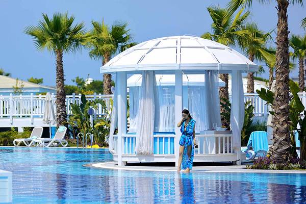 Eine Frau in einem blauen Badeanzug steht vor einem weißen Pavillon am Pool der Sueno Hotels Deluxe Belek.