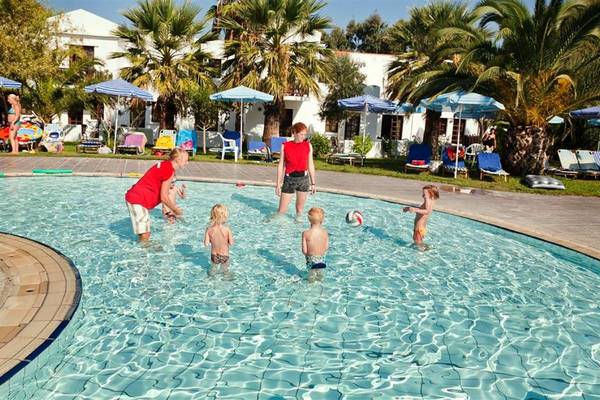 Kinder schwimmen im Pool im Atlantica Marmari Beach Hotel mit Sonnenschirmen und Liegestühlen im Hintergrund.