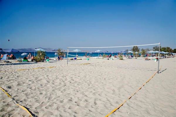 Ein Volleyball-Netz auf einem sandigen Strand mit Gästen und Sonnenschirmen.