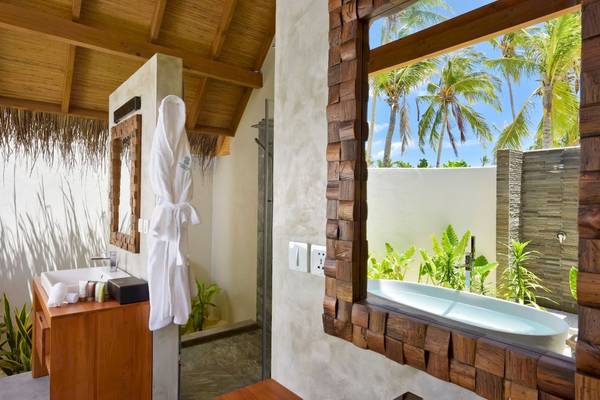 Badezimmer im Fushifaru Maldives Hotel mit Aussicht auf den Garten und Palmen.