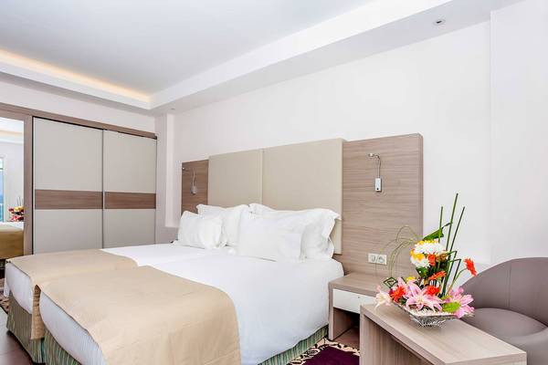 Schlafzimmer im Atlas Amadil Beach Hotel mit zwei Betten, weißen Kissen und einem Nachttisch mit Blumenvase.