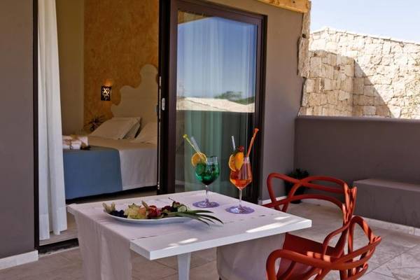 Balkon mit Tisch, zwei Cocktails, Dessertteller und Blick auf ein Bett im Hintergrund